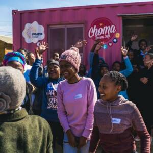 Group of laughing young people in front of a pink Choma Dreams Caf trailer